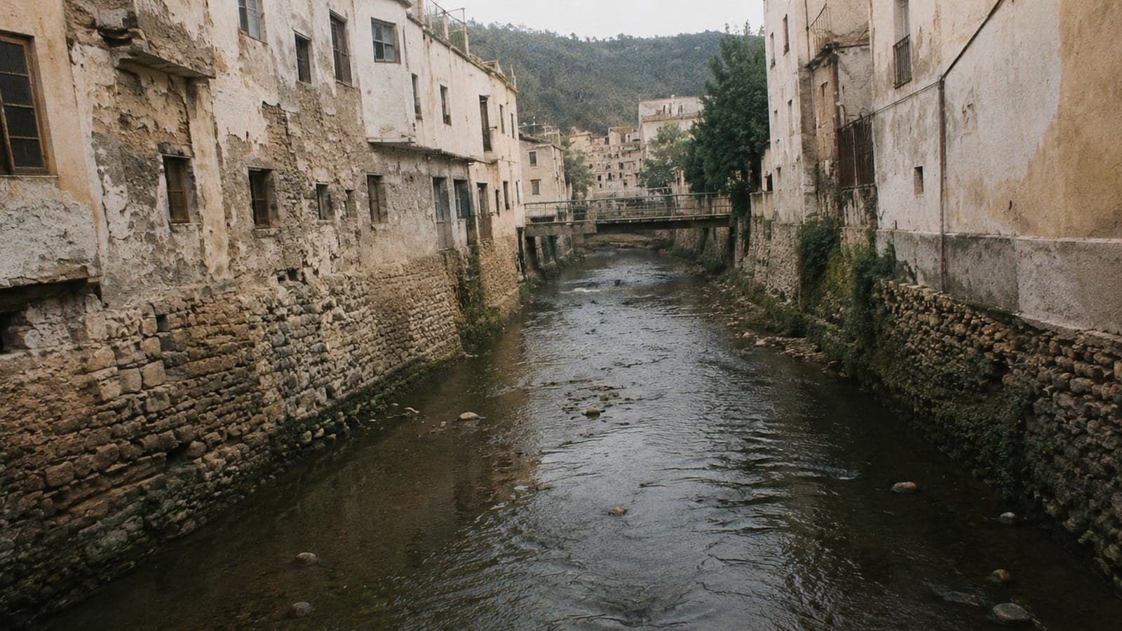 נהר צר בין בתי אבן וטיח בעיירה מרוקאית, גשר קטן ברקע
